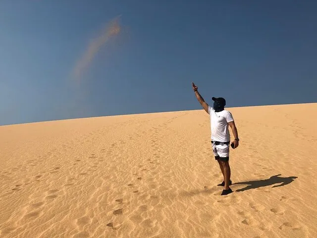 A person throwing sand into the air on a vast desert dune