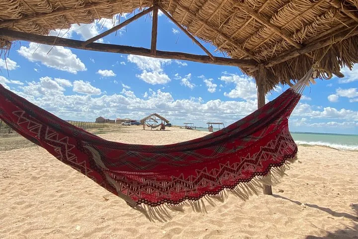 A traditional red hammock under a thatched roof on a sandy beach