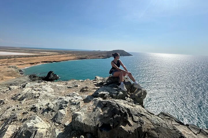 A woman sitting on a rocky cliff overlooking the ocean and coastline